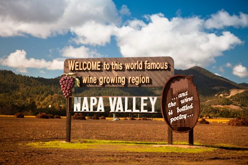 Sign welcoming visitors to Napa Valley, a renowned wine-growing region, with scenic hills and blue skies in the background.
