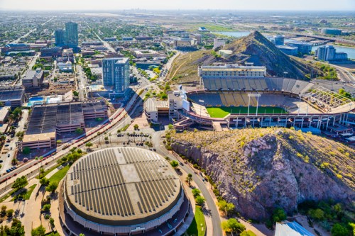 Aerial view of a cityscape featuring stadiums, buildings, and mountains in the background under a clear sky.