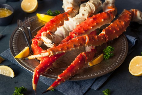 A platter of cooked crab legs garnished with lemon wedges and parsley, set on a dark table.