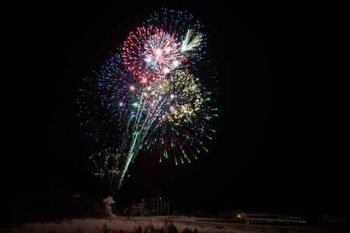 Colorful fireworks burst in the night sky over a snowy landscape, illuminating the darkness with vibrant hues.