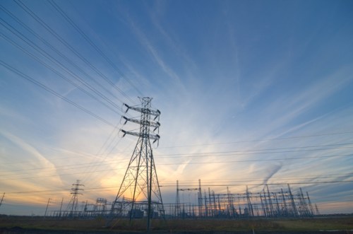 Silhouetted power lines and towers against a colorful sunset sky with wispy clouds.