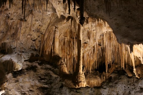 Stalactites and stalagmites in a dimly lit cave, showcasing intricate rock formations and textures.
