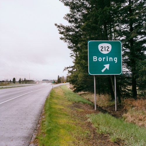 A green highway sign indicating a right turn for Boring, with a wet road and trees in the background.