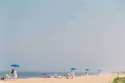 A serene beach scene with lifeguard towers and umbrellas, stretching along the sandy shore under a hazy sky.