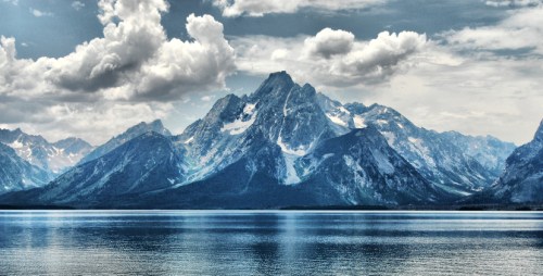 A serene mountain landscape with snow-capped peaks reflecting in a calm lake under a cloudy sky.