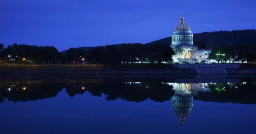 The West Virginia State Capitol illuminated at night, reflecting in the water below.