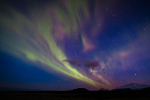 A vibrant aurora borealis dances across a starry night sky, with mountains silhouetted below.