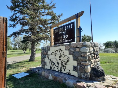 Sign for Spring Lake Park, featuring a stone base and a tree in the background, set in a grassy area.