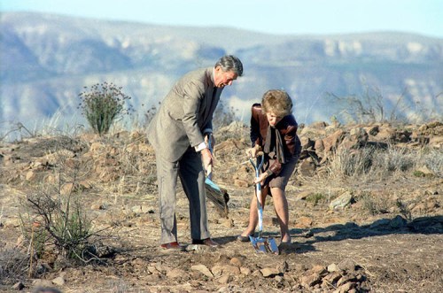 Former President Ronald Reagan and First Lady Nancy Reagan digging in the ground with shovels in a rocky landscape.