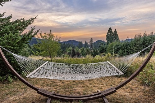 A hammock suspended between wooden supports, set against a backdrop of trees and mountains at sunset.