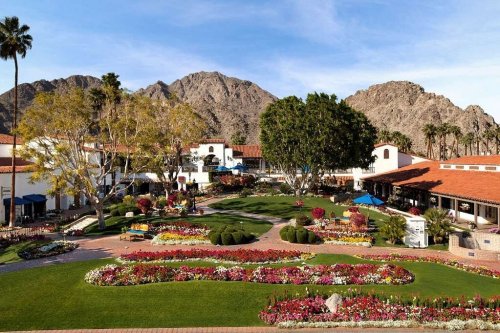 A scenic view of a landscaped garden with colorful flowers, palm trees, and mountains in the background.