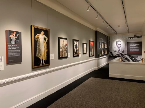 A gallery wall featuring framed artworks and informational panels about advertising art.