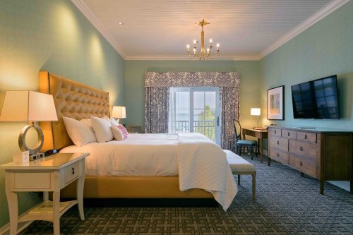 A stylish hotel room featuring a large bed, elegant decor, a TV, and a view through a window with sheer curtains.