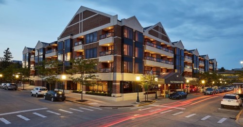 Modern hotel exterior at dusk, featuring balconies, trees, and cars on a street with light trails.