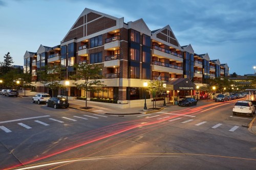 A modern hotel building at dusk, featuring balconies and streetlights, with light trails from passing cars.