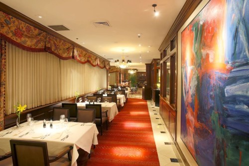 Elegant restaurant interior with tables set for dining, colorful artwork, and warm lighting.