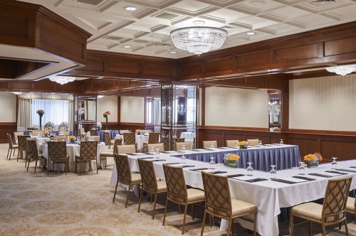 Elegant meeting room with wooden accents, round tables, and floral centerpieces, featuring chandeliers and soft lighting.