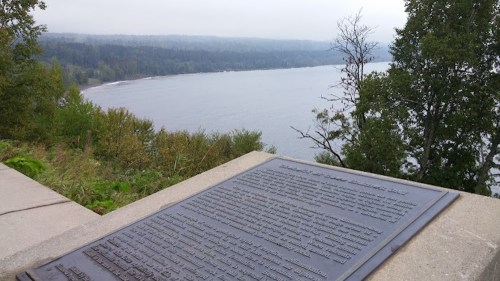 A plaque overlooking a misty river and forested shoreline, with trees framing the view in the background.