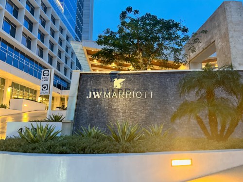 The JW Marriott hotel entrance at dusk, featuring a stone sign and lush greenery.