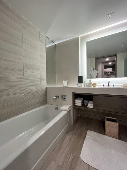 Modern bathroom featuring a bathtub, large mirror, and a vanity with towels and toiletries. Neutral color scheme.