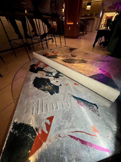 A partially rolled-up rug with colorful abstract designs, placed on a tiled floor in a dimly lit bar setting.