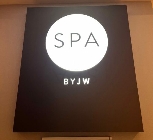 Illuminated sign for "SPA BYJW" on a wall, featuring a circular design with the word "SPA" prominently displayed.