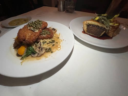 Two gourmet dishes on white plates: one with breaded chicken, pasta, and capers; the other a meat pie with greens.