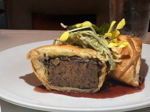 A slice of pastry filled with dark, rich filling, garnished with greens and edible flowers on a white plate.