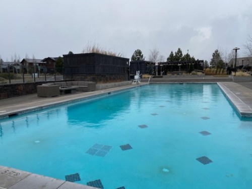 A cloudy day at an outdoor pool surrounded by lounge chairs and a wooden structure in the background.