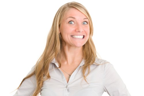 A smiling woman with long blonde hair, wearing a light gray shirt, poses cheerfully against a white background.
