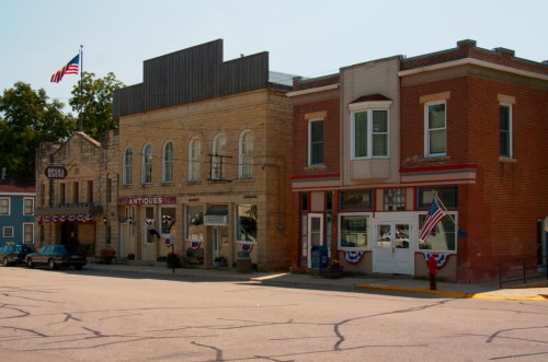 Historic buildings with American flags, featuring an antique shop and a brick storefront, on a sunny day.