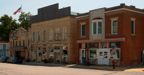 A quaint street scene featuring antique shops and patriotic decorations, with an American flag waving overhead.