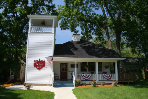 A charming white café with a bell tower, decorated with red, white, and blue bunting, surrounded by greenery.