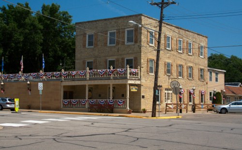 Historic stone building decorated with red, white, and blue bunting, located at a street intersection on a sunny day.