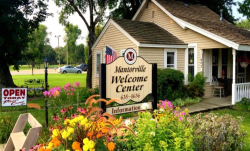 A charming welcome center with a sign, flowers, and an American flag, set in a green landscape.
