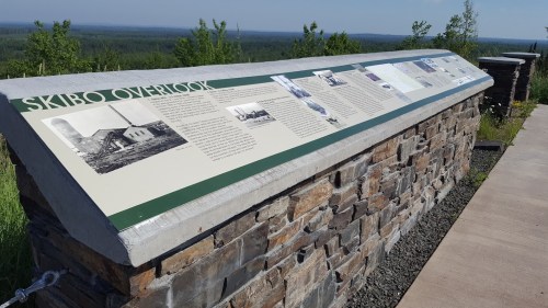 A stone overlook display with historical information and scenic views of a forested landscape in the background.