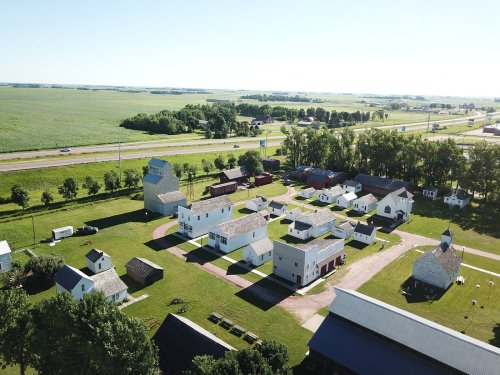 Aerial view of a rural village with white buildings and green fields, near a highway.