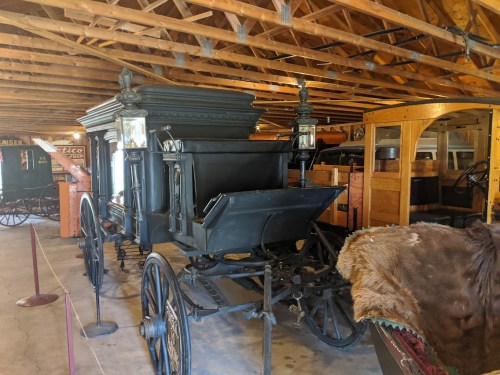 A vintage horse-drawn carriage displayed in a wooden barn, featuring lanterns and intricate details.