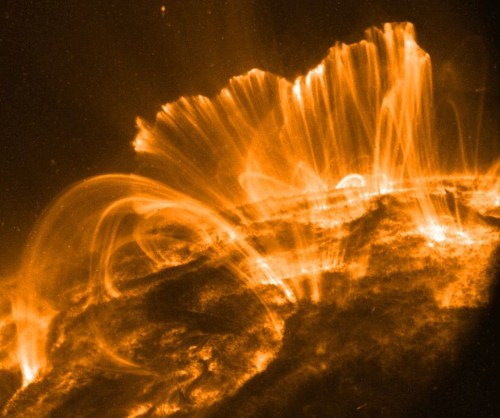 A close-up view of solar flares and plasma arcs on the sun's surface, glowing in vibrant orange hues.