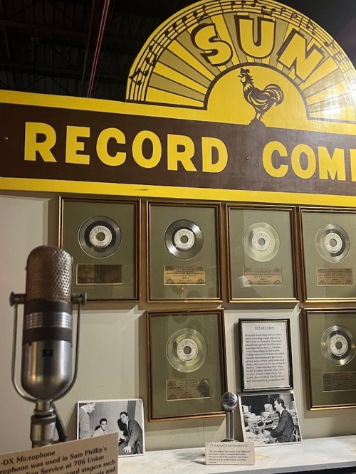 A vintage microphone in front of a display featuring gold records at Sun Record Company.