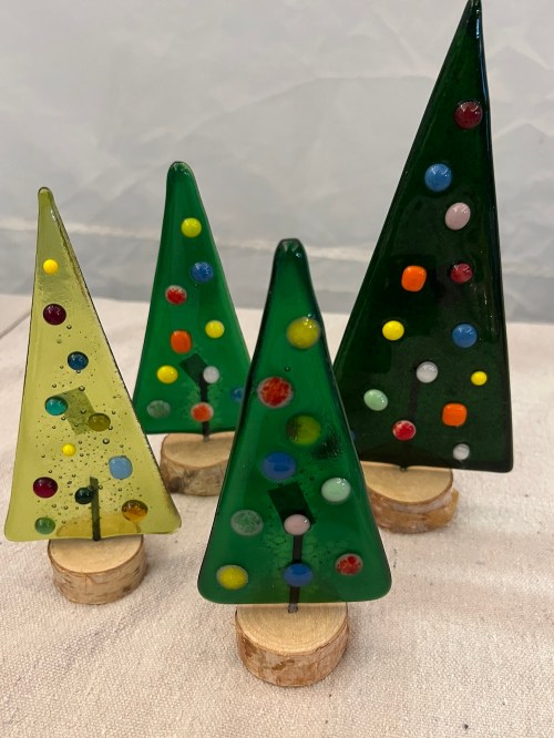 Four decorative glass Christmas trees in green and yellow, adorned with colorful dots, resting on wooden bases.