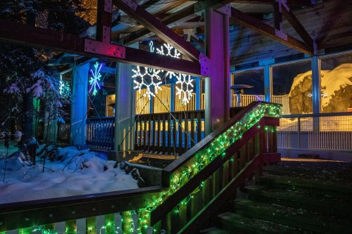 A snowy outdoor scene featuring colorful holiday lights and decorations on a wooden staircase and railing.