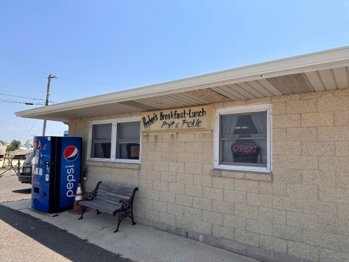 A small diner with a sign reading "Maggie's Breakfast-Lunch" and a Pepsi vending machine outside.