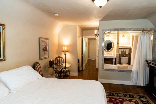Cozy bedroom with a bed, small dining table, and an open bathroom area featuring a shower and sink.