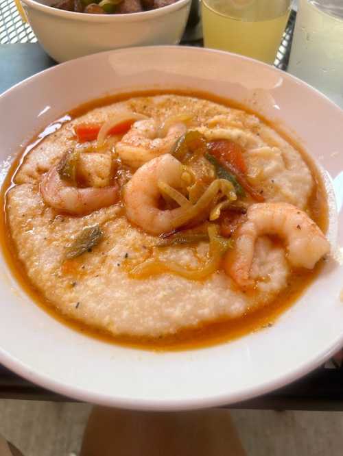 A bowl of shrimp and grits topped with sautéed vegetables in a savory sauce.