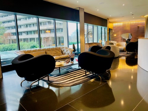 Modern lounge area with stylish black chairs, a beige sofa, and large windows overlooking greenery.