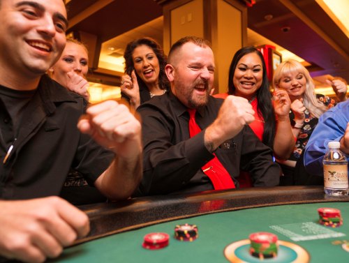 A group of excited people celebrating at a casino table, with chips and cards in front of them.