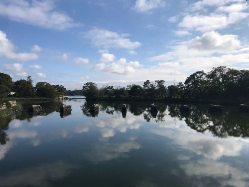 A serene landscape featuring a calm lake reflecting clouds and trees under a blue sky.