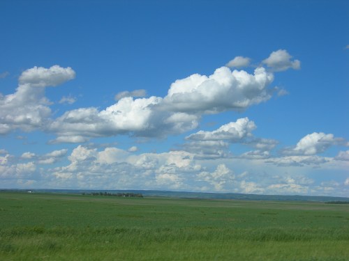 A vast green landscape under a bright blue sky filled with fluffy white clouds.