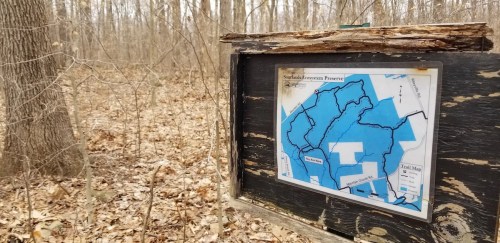 Trail map at a wooded area, showing paths and features of the surrounding nature preserve. Trees in the background.